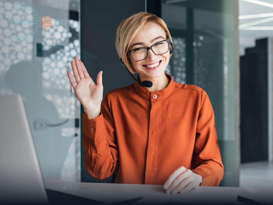 Smiling support agent with a headset waving on a video call
